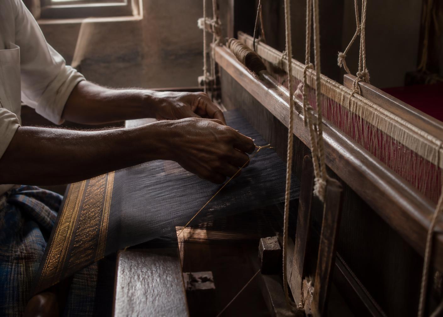 Handloom weaver working gold zari threads on a wooden pit loom